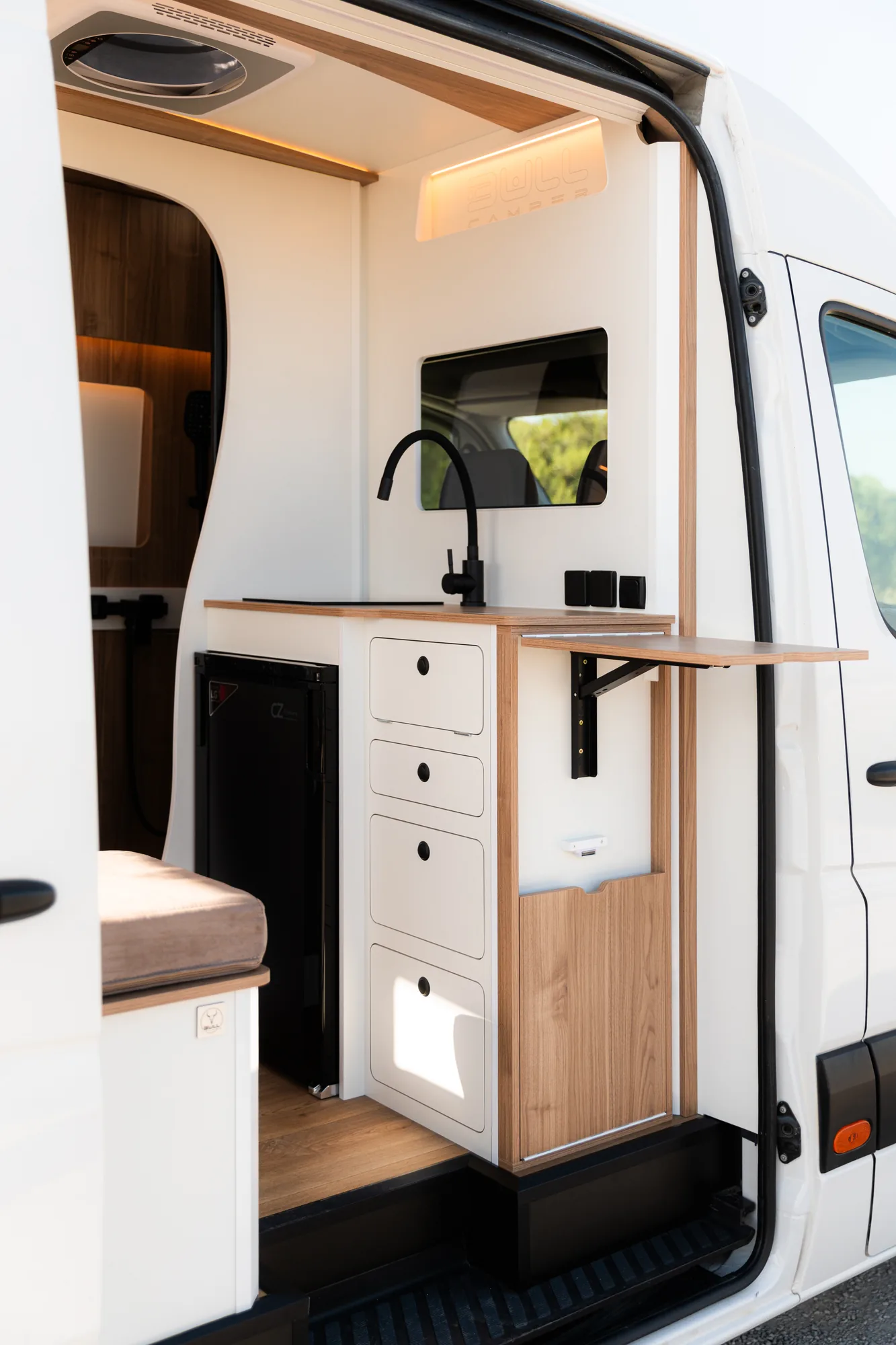Volkswagen Crafter camperizada vista desde la puerta lateral, con mueble de cocina blanco, fregadero y mesa abatible