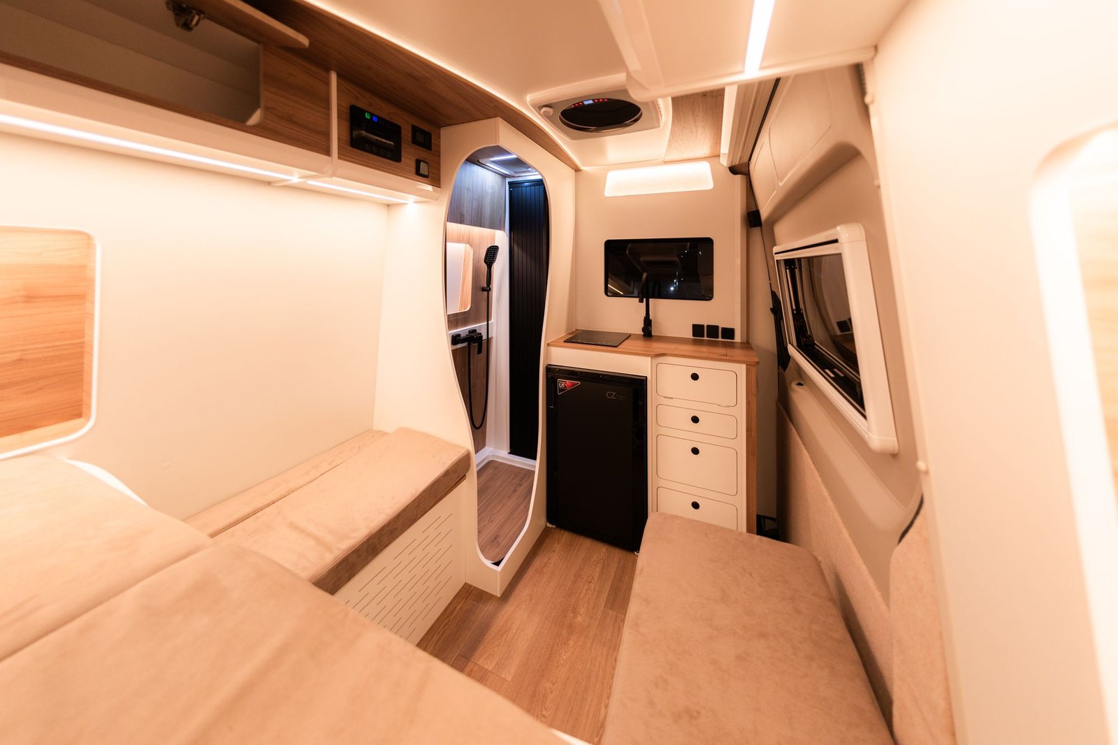 Interior en blanco y madera con sofá cama, mueble de cocina con cajones y puerta curva del baño