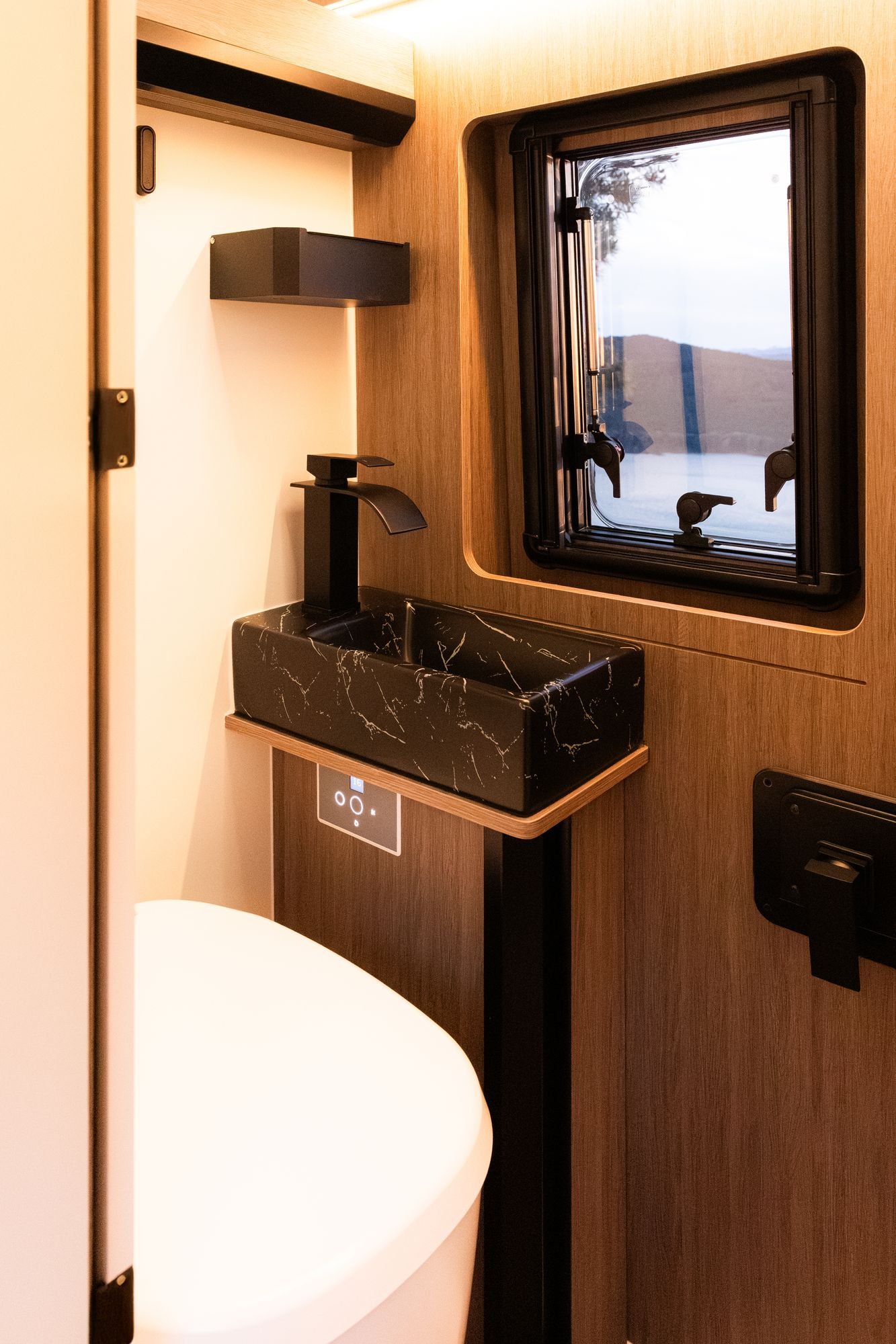 Baño de la camper con lavabo de mármol negro, grifo negro y ventana con vistas al embalse