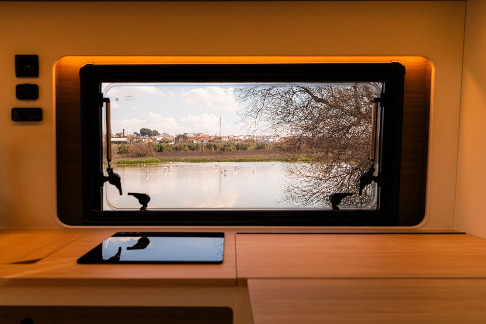 Ventana con marco iluminado sobre la encimera de madera con placa de inducción y vistas a una laguna