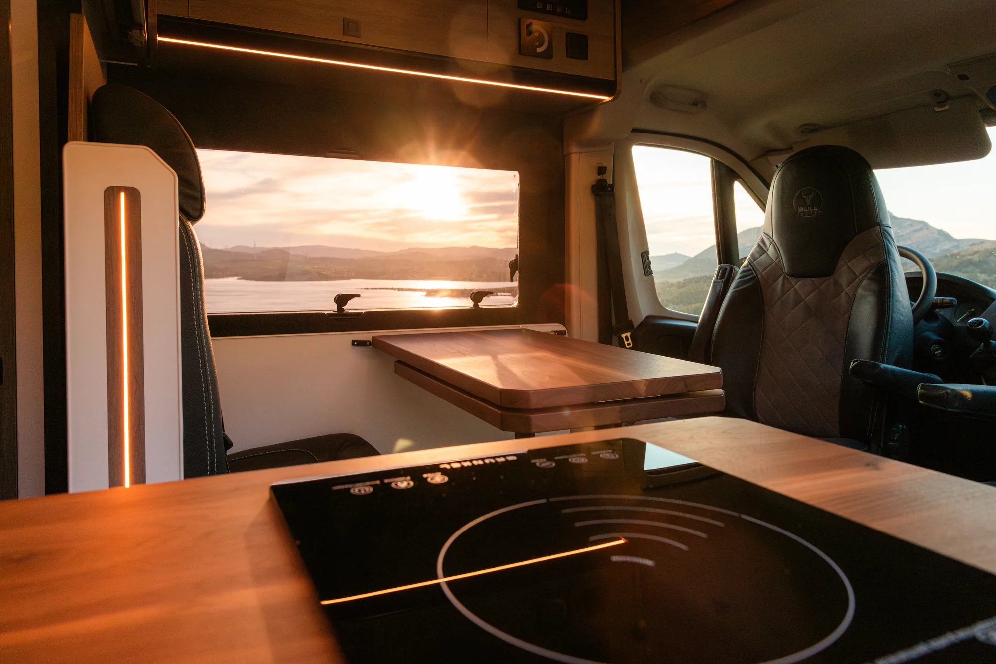 Encimera de madera con placa de inducción y mesa plegable junto a la ventana al atardecer