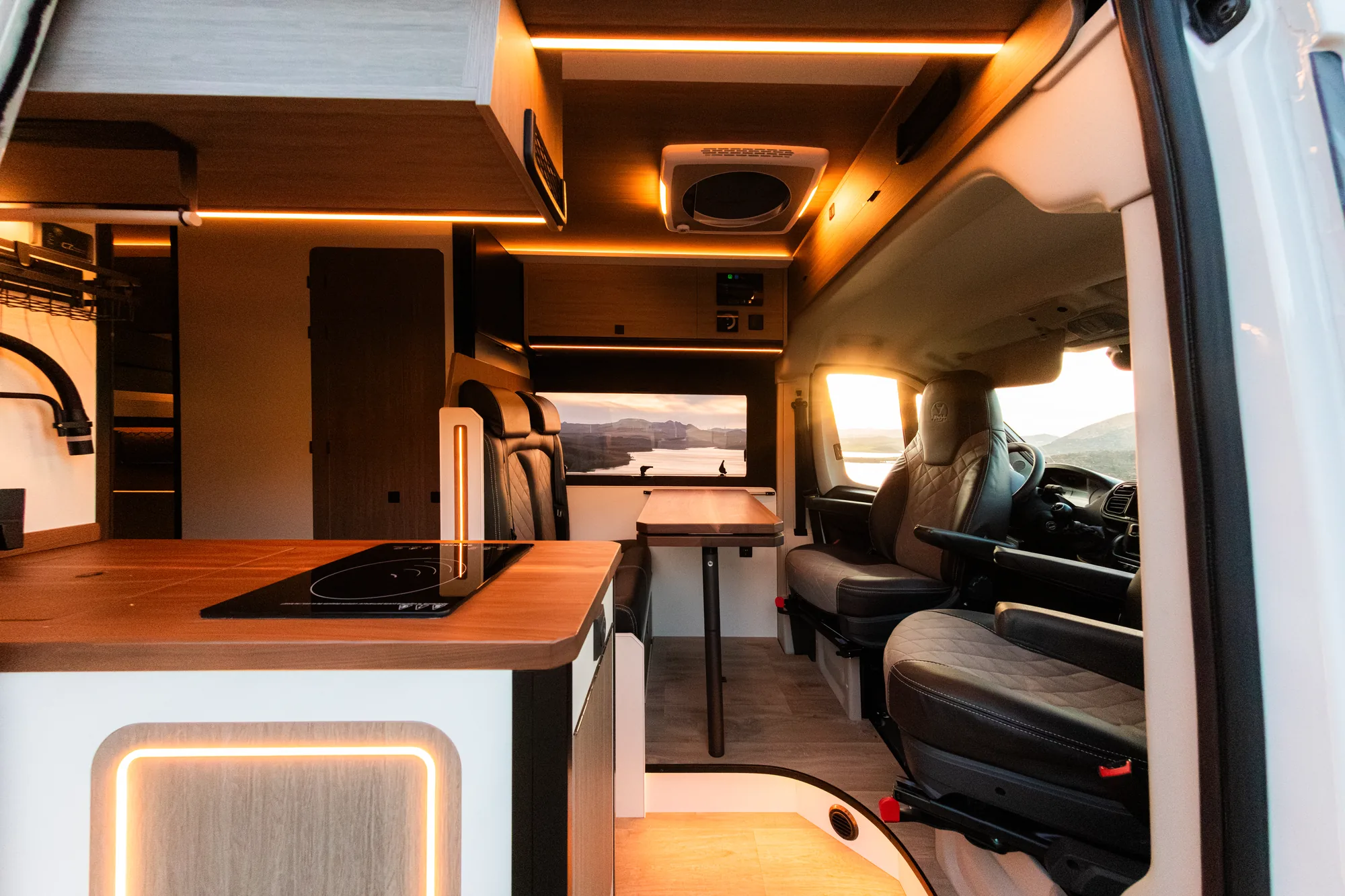 Vista del interior hacia la cabina con cocina, mesa y asientos giratorios iluminados con LED