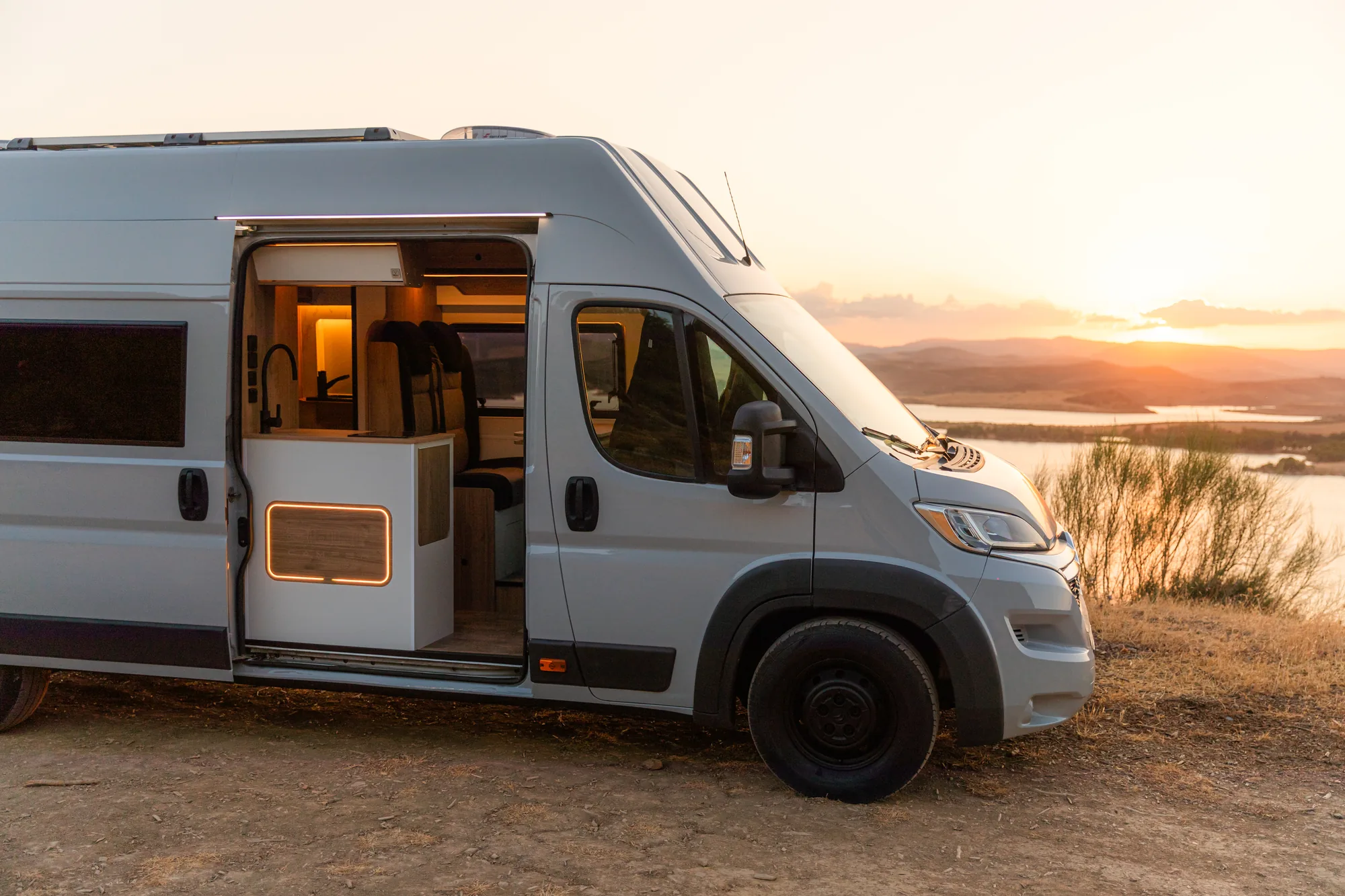 Citroën Jumper camperizada con la puerta lateral abierta frente a un embalse al atardecer