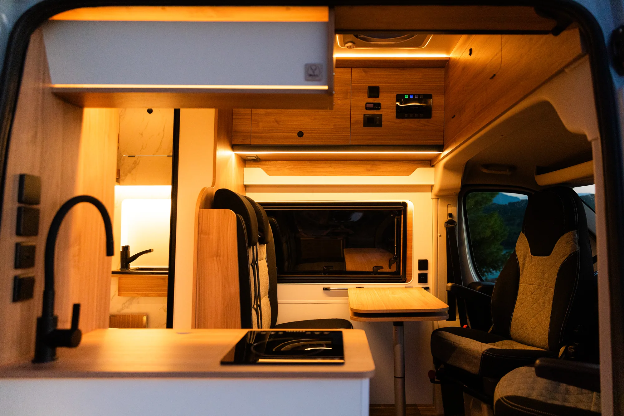 Cocina con grifo negro y placa de inducción frente a los asientos giratorios de la cabina
