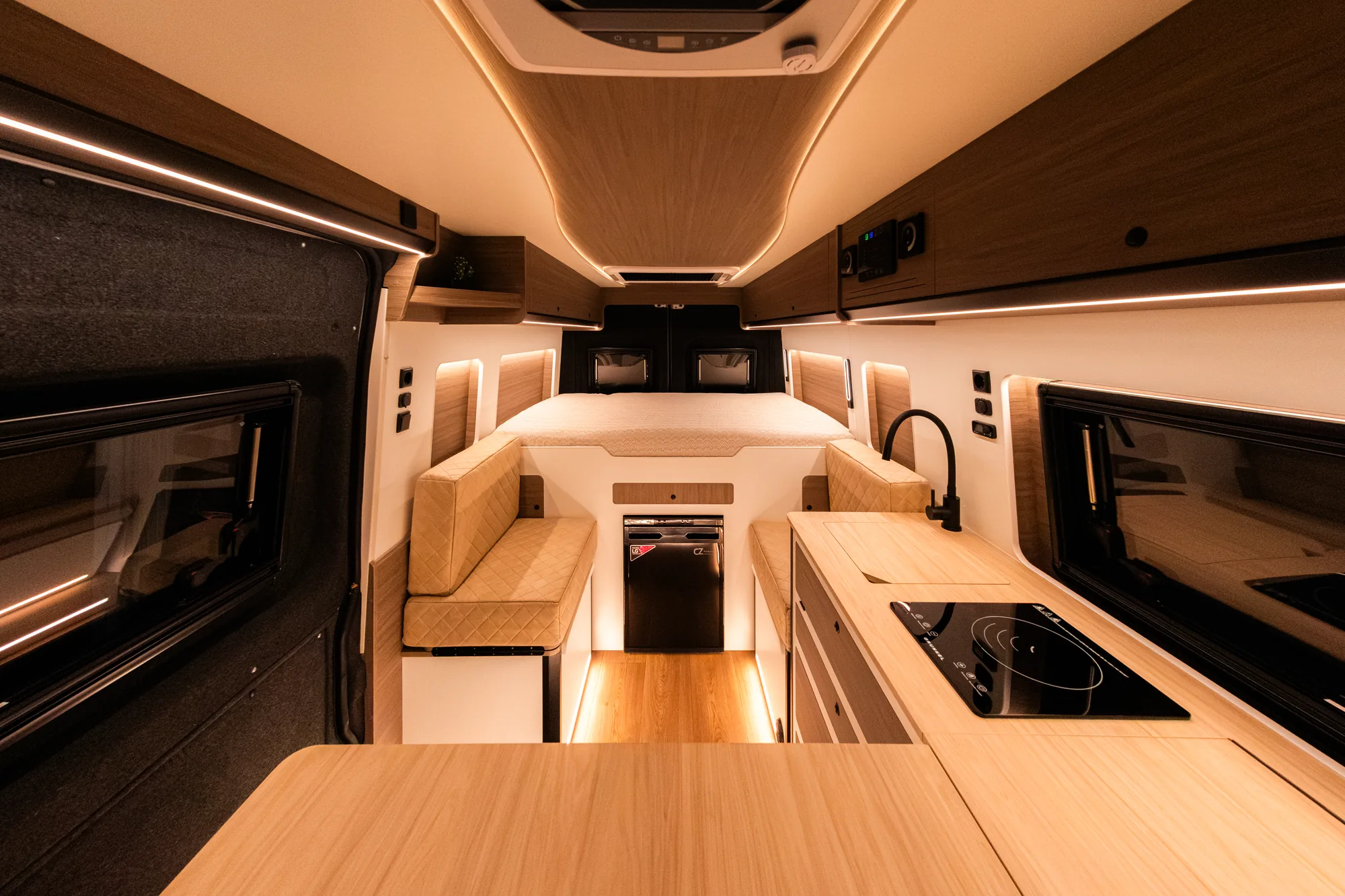 Interior de camper Opel Movano con cocina de inducción, salón con bancos tapizados e iluminación LED indirecta
