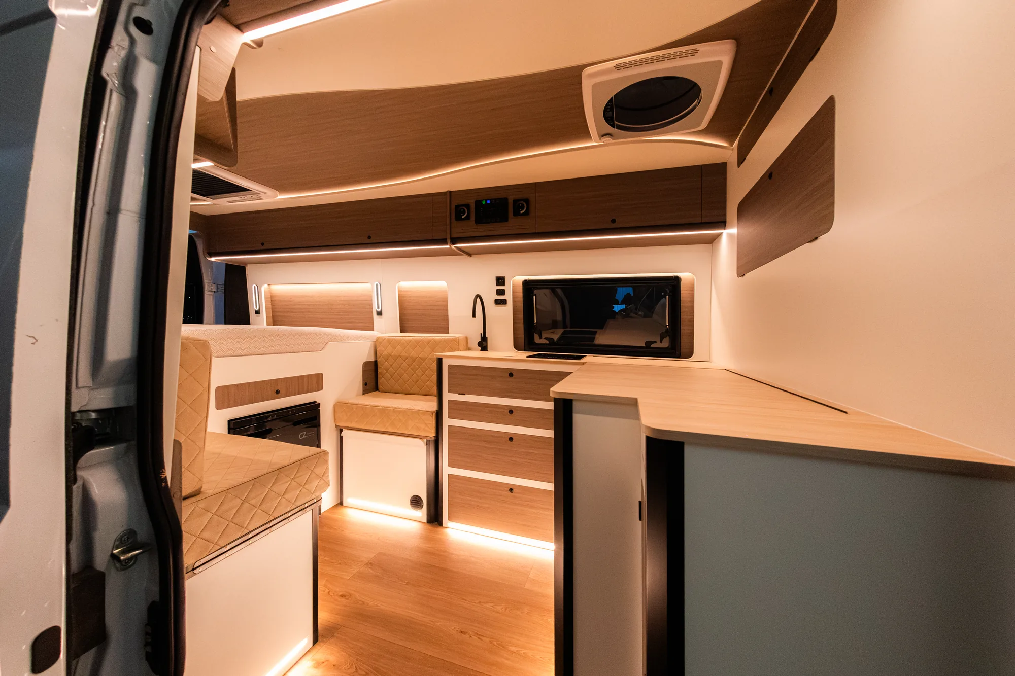 Interior de la Opel Movano visto desde la puerta lateral, con cocina, salón y suelo de madera